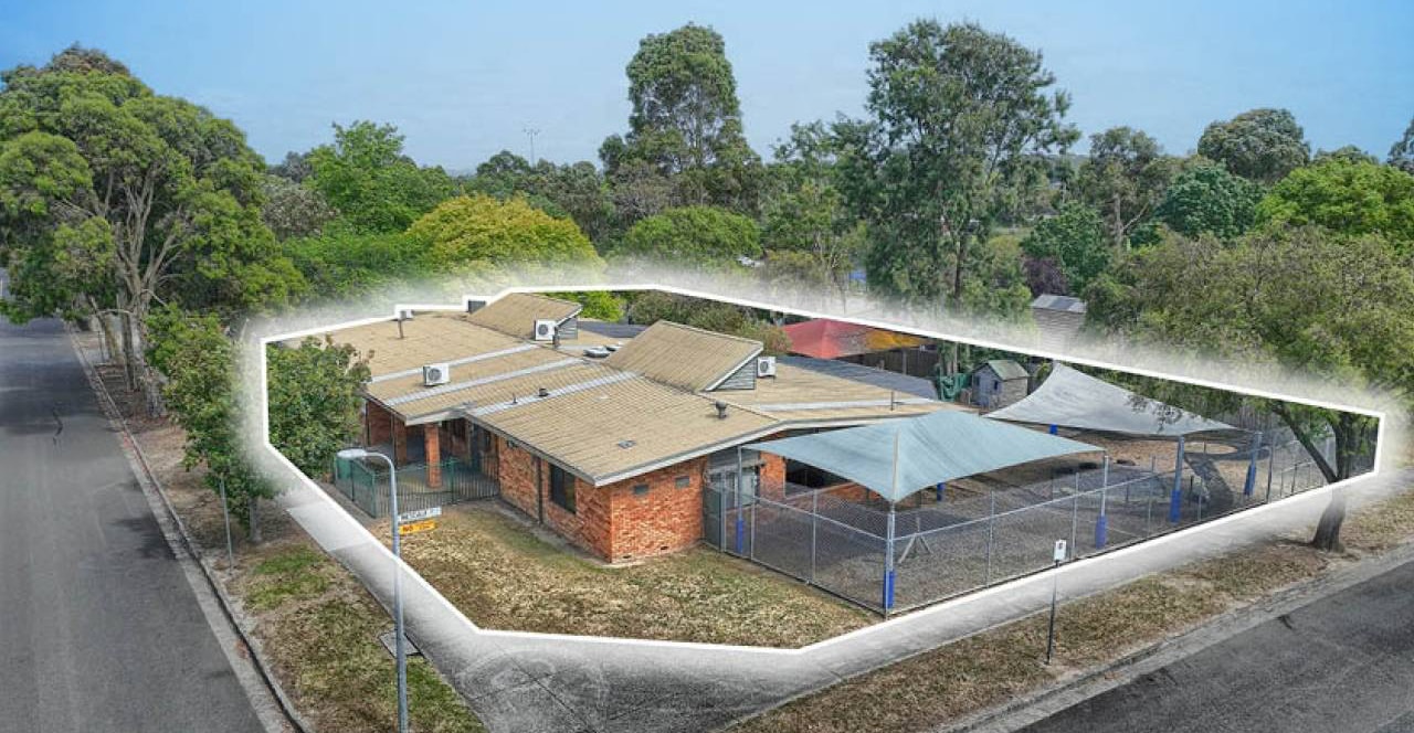 Aerial view of the site with the title boundary marked in white, showing the building, play yards and two street frontages.