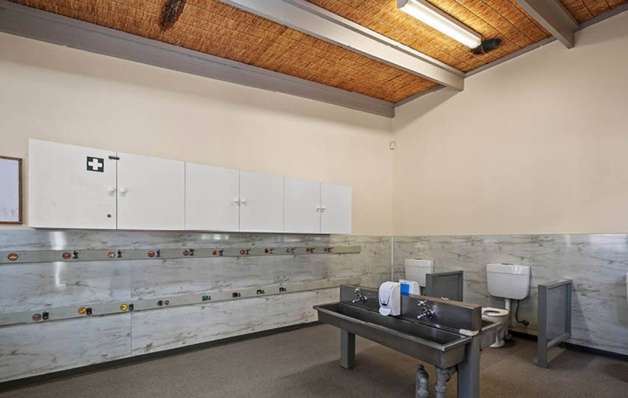Children's bathroom with a stainless trough basin, low toilet pans and a wall-mounted first aid cabinet.