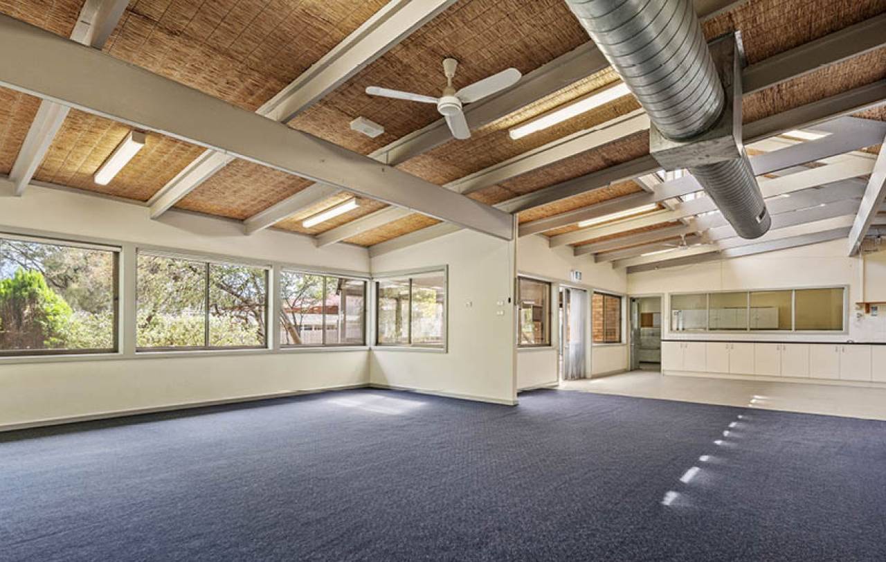 Carpeted corner room with windows to two elevations and exposed beams overhead.